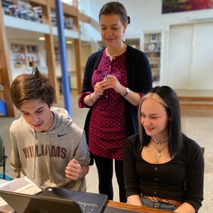 two students and a teacher looking at a laptop