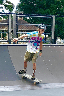 A Rock Point School student rides a skateboard down a quarter pipe at a skate park in Burlington, Vermont. The student is male presenting, wearing a tie-dye shirt.