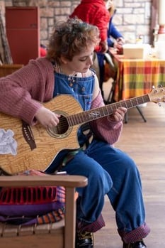 a Rock Point School student sits on the porch outside the front of the building and plays guitar.