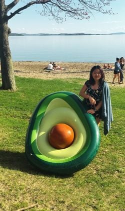 A Rock Point School student is at the beach on the shores of Lake Champlain in Burlington, Vermont, holding a large floatation device that looks like a cut open avocado.