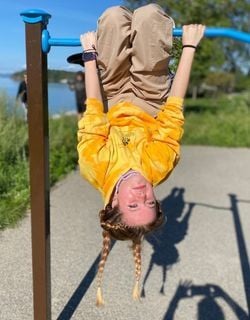 A Rock Point School student wearing a tie-dye yellow sweatshirt and khaki pants hangs upside down on the monkey bars at a park near Lake Champlain in Burlington, Vermont.