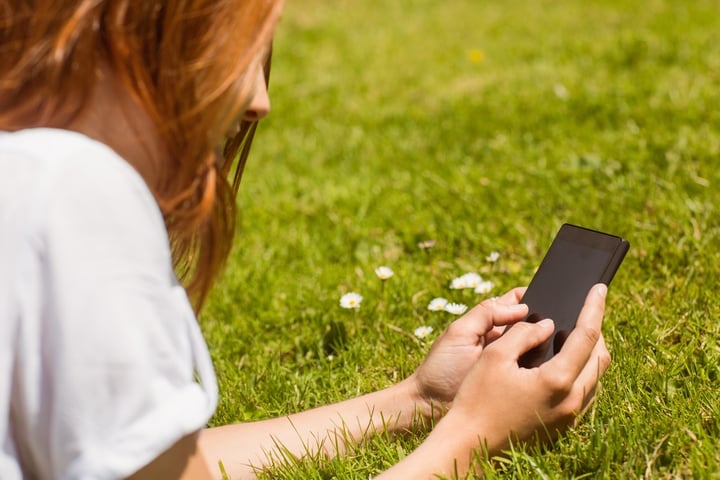 Pretty redhead text messaging on her phone lying on grass.jpeg