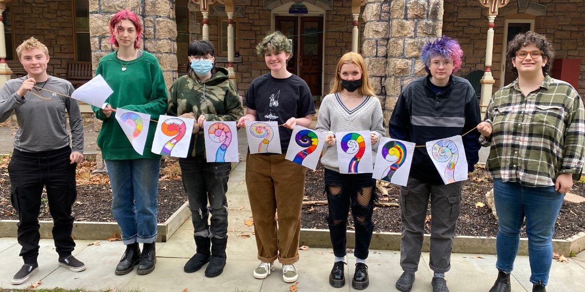 Group of students standing out front at Rock Point School holding up rainbow colored art. 